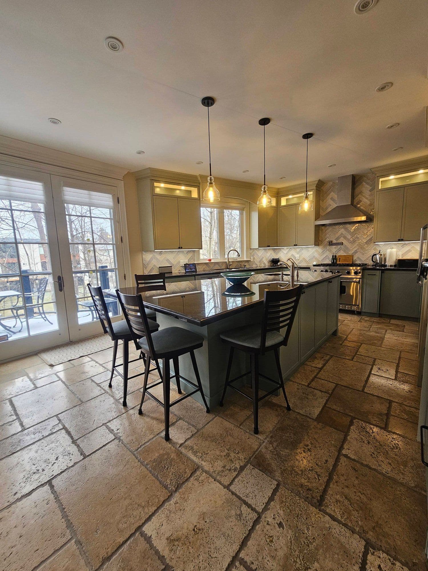 Kitchen with sage green cabinetry, travertine flooring, and herringbone backsplash