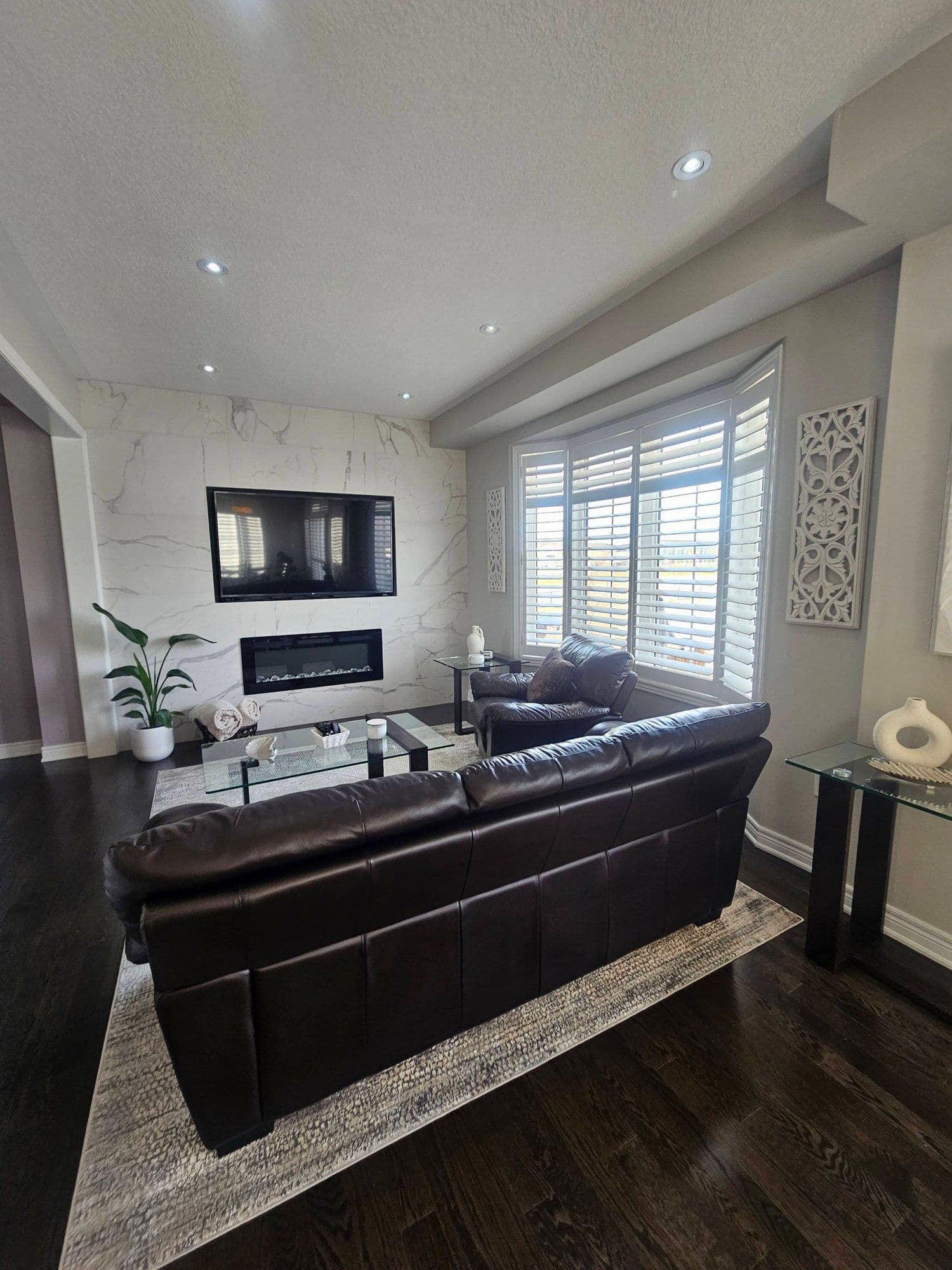 Living room with marble fireplace, leather sofas, and plantation shutters